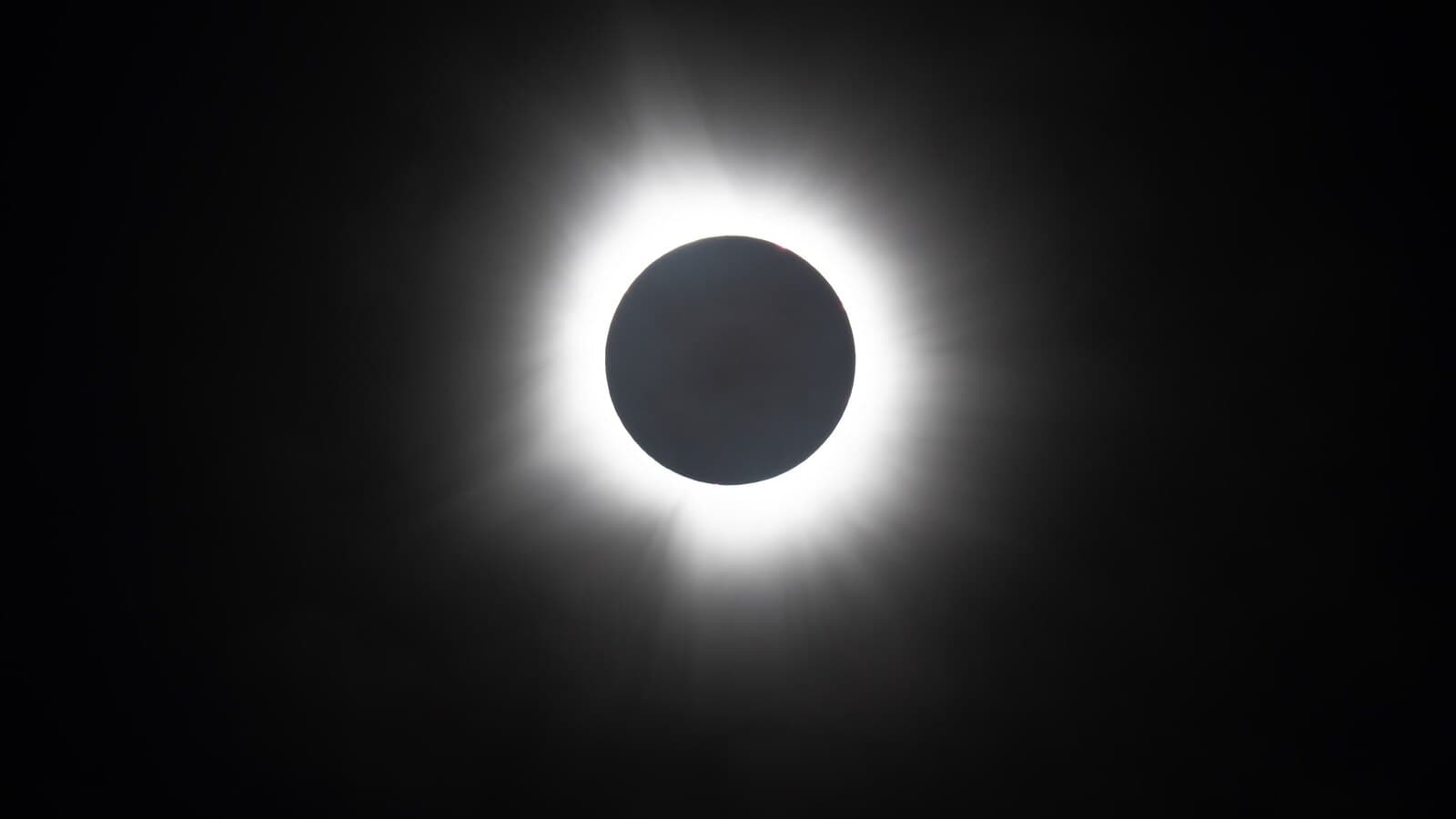 The sun's white corona around the black disc of the moon during a total solar eclipse.