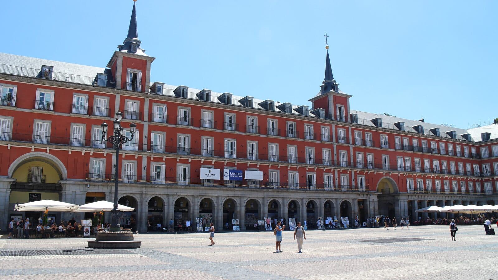 The red arcaded façades and spires of the Plaza Mayor in Madrid under a clear sky.